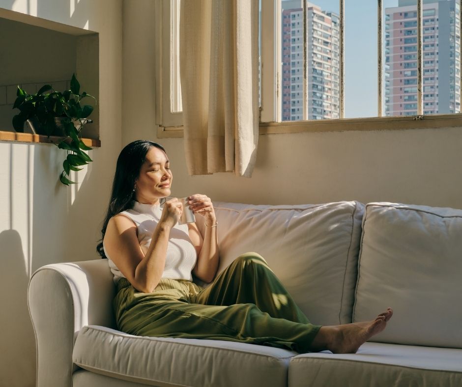 A woman sits on the couch with her eyes closed