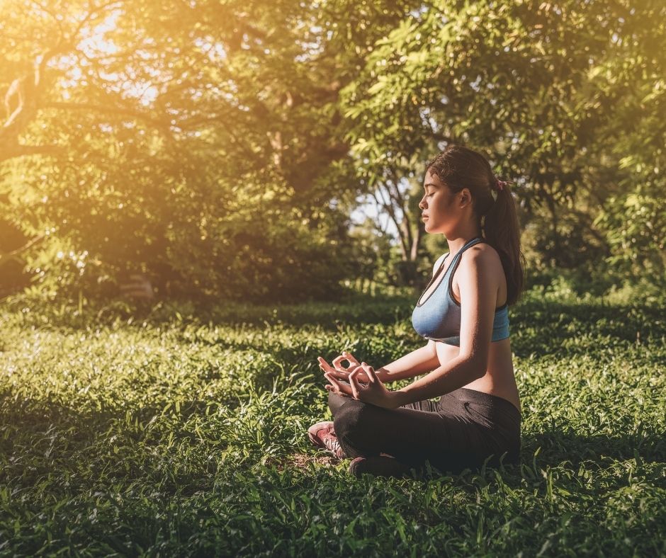 A woman sitting cross-legged in the grass meditates