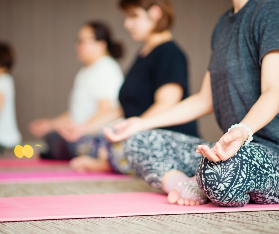 Una fila de personas sentadas con las piernas cruzadas sobre esterillas de yoga y meditando.