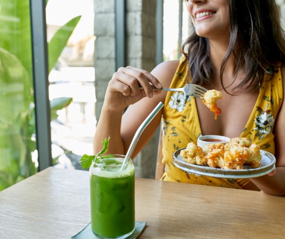 Una mujer sentada a la mesa a punto de comer un plato de camarones y un jugo verde.
