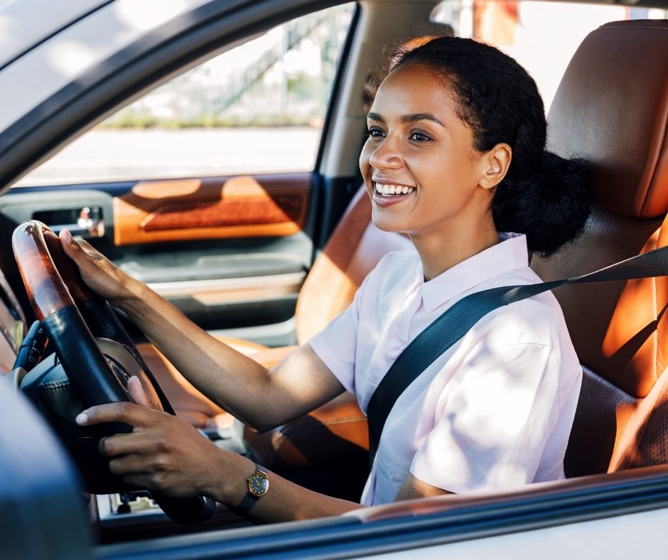Una mujer latina sonriente al volante de un coche.