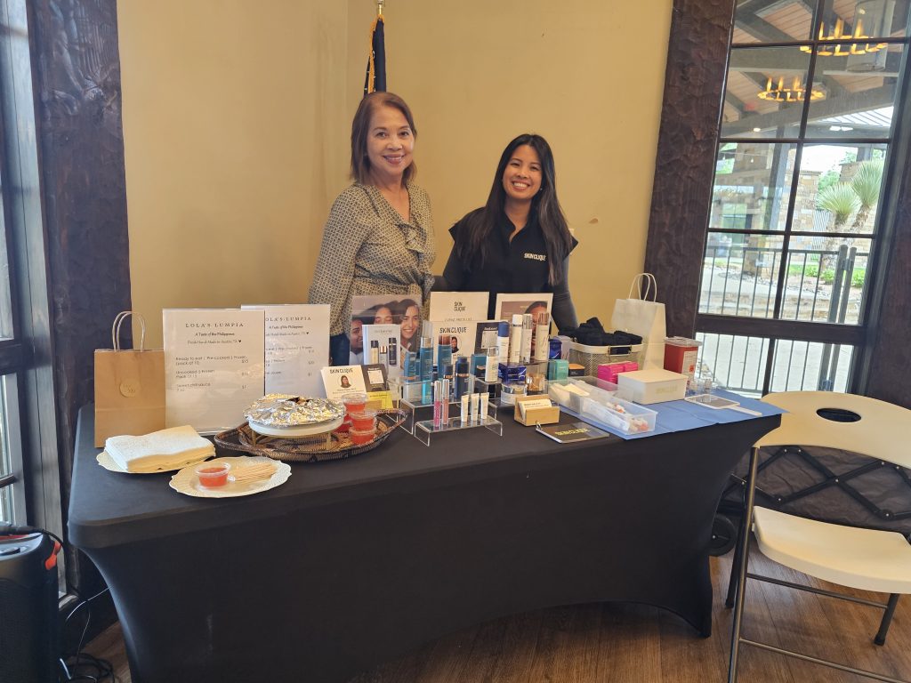 Dos empresarias locales sonrientes posan detrás de su mesa en un evento para recaudar fondos en Austin, Texas.