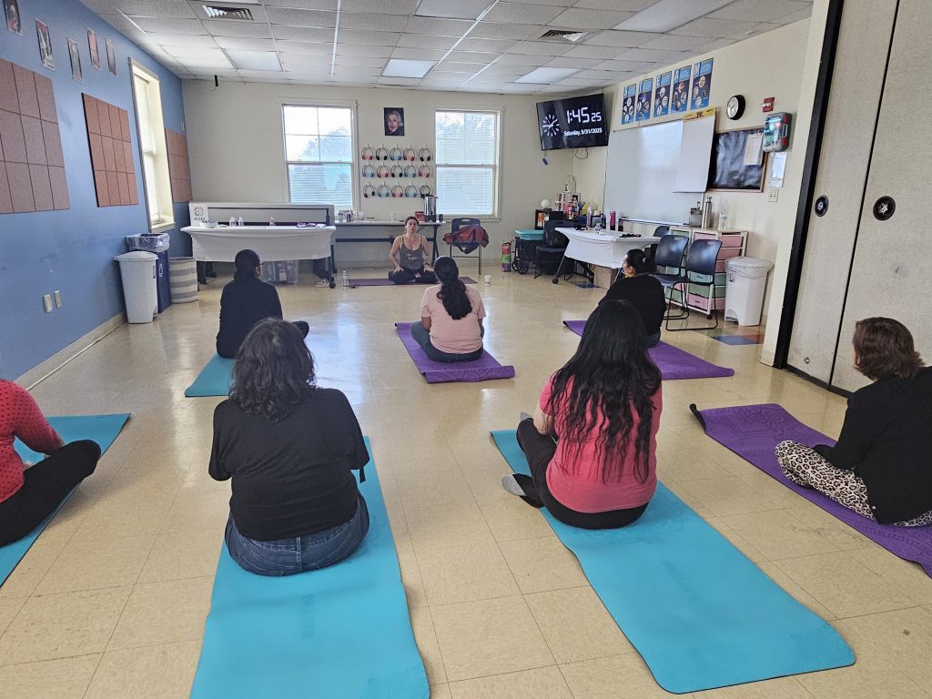 Un grupo de mujeres latinas en un taller de empoderamiento realizando una clase de yoga.