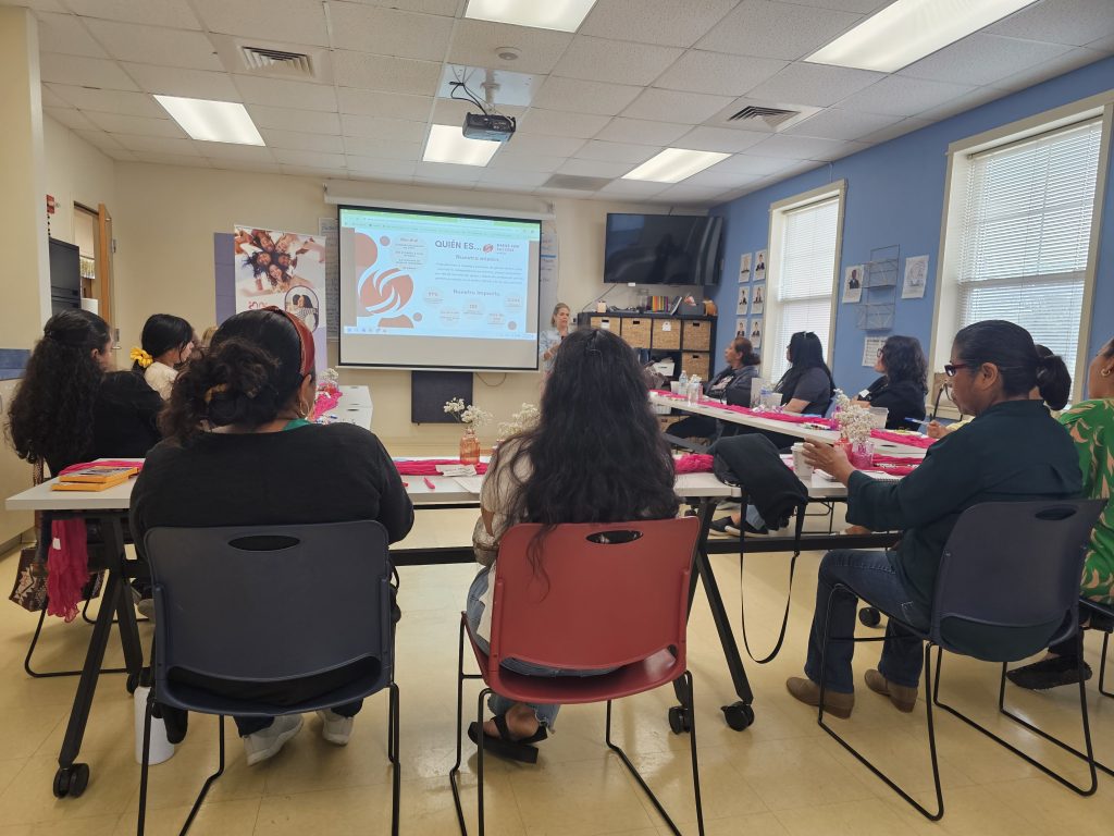 Un grupo de mujeres latinas sentadas alrededor de una mesa escuchando una presentación de Dress for Success.
