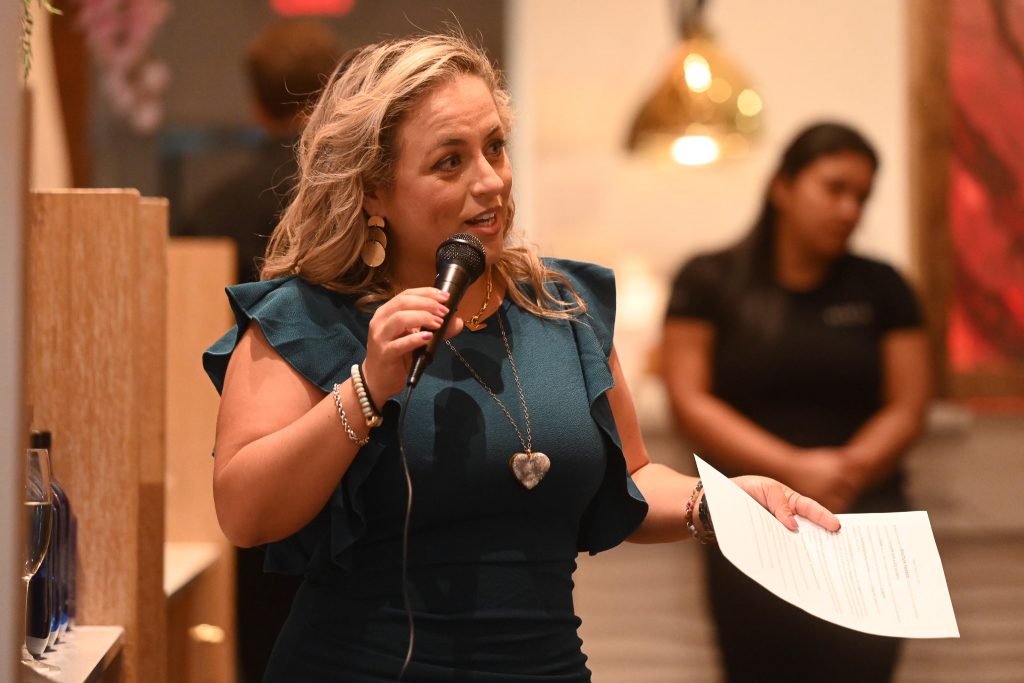 Mujer latina bien vestida con un micrófono dando un discurso en un evento para recaudar fondos.