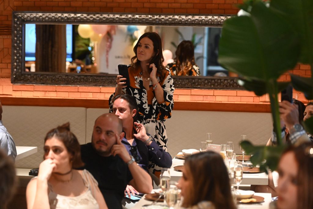 Personas elegantemente vestidas sentadas en un evento de recaudación de fondos en un restaurante escuchando un discurso.
