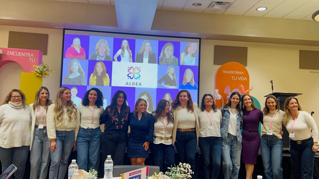 Un grupo de mujeres latinas que forman parte del personal y son voluntarias de la organización sin fines de lucro Aldea se hacen una foto en un evento.
