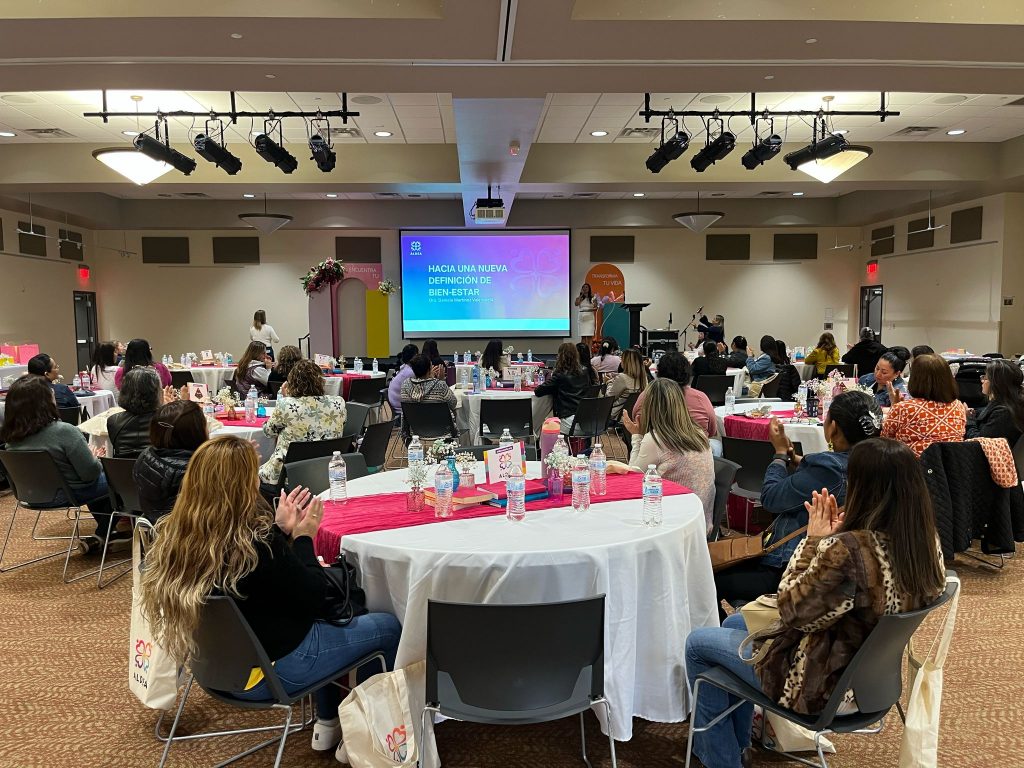 Women sitting around tables during an event looking at a powerpoint presentation at the front of the room